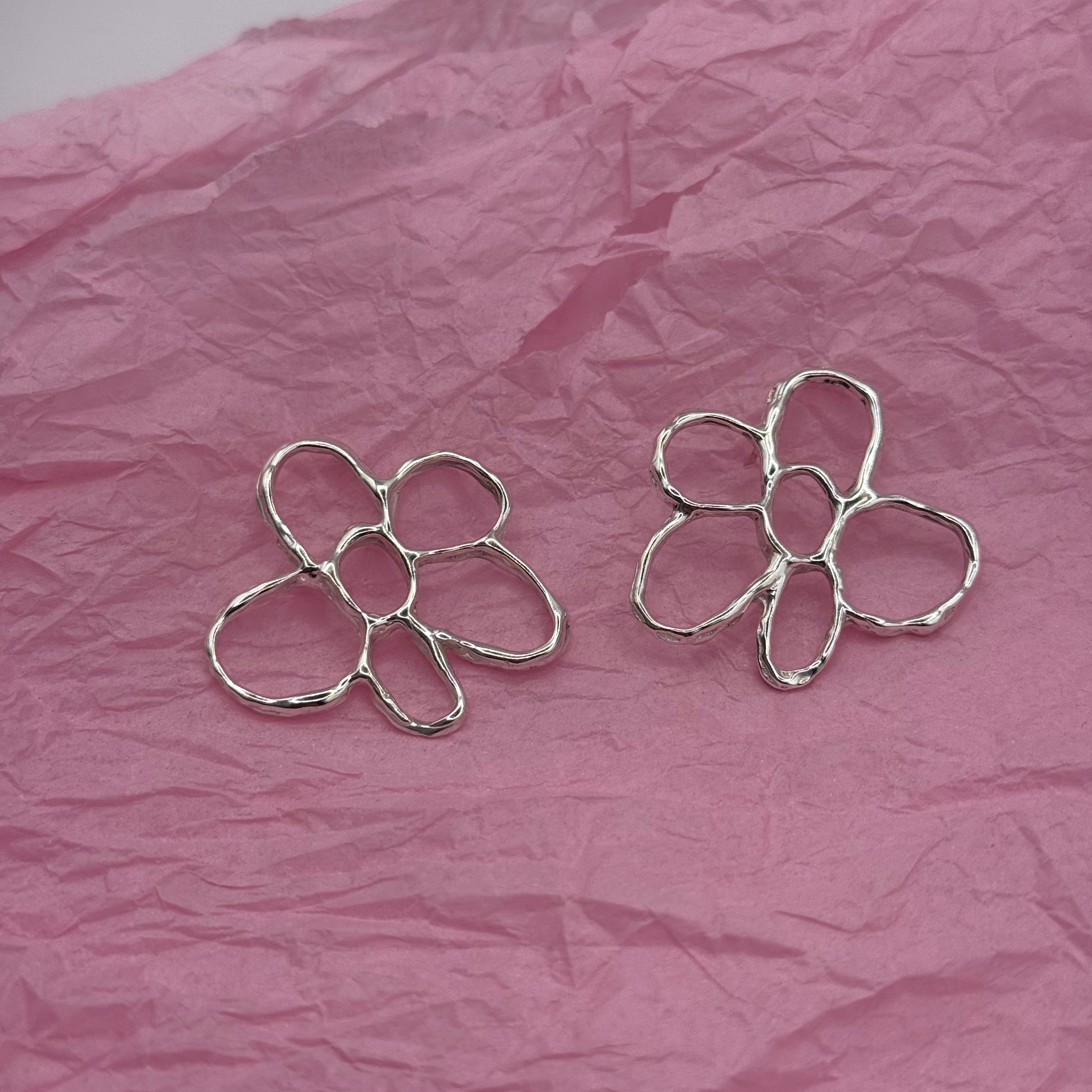 Silver flower-shaped earrings on a pink crumpled paper background